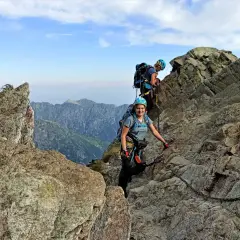 Dwoje turystów wspina się po skalistych tatry wysokie szlaki, korzystając z łańcuchów. Widok na góry i błękitne niebo.