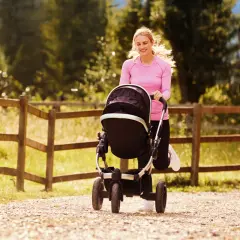Uśmiechnięta kobieta w różowej bluzie pcha wózek na Rusinowej Polanie.