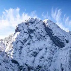 Ośnieżony szczyt Giewontu z krzyżem, pod błękitnym niebem z pierzastymi chmurami. Zastanawiasz się, ile trwa wejście na Giewont?