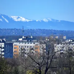 Widok na krakowskie bloki i wieżowiec. W oddali, na horyzoncie, widać ośnieżone szczyty Tatr.