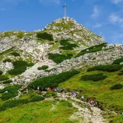 Tłum turystów podąża kamienistą trasą na Giewont. W oddali widać szczyt z krzyżem.