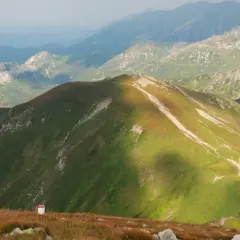 Widok na Tatry z Kopy Kondrackiej. Szlak turystyczny wije się po zielonych zboczach, a w oddali widać kolejne pasma górskie.