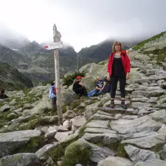 Kobieta w czerwonej kurtce na kamienistym szlaku. W oddali góry i chmury. Wrota Chałubińskiego szlak.