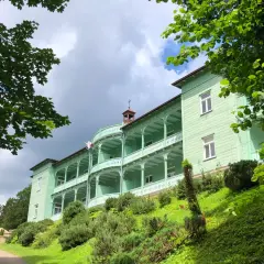 Zielony, zabytkowy klasztor w Komańczy, otoczony bujną zielenią, z charakterystycznymi werandami i białymi balustradami.