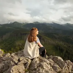 Kobieta siedzi na skale, podziwiając widok na góry. Szlak na Nosal widać w oddali.