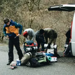 Grupa młodych ludzi przygotowuje się do wycieczki w Tatry, pakując plecaki i sprzęt przy otwartym bagażniku białego vana.