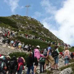 Tłum turystów podąża czerwonym szlakiem na Giewont. W oddali widoczny krzyż na szczycie.