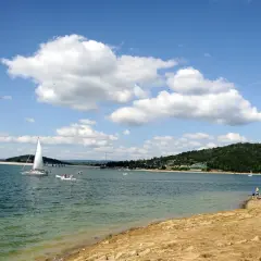 Słoneczna plaża nad Soliną, z żaglówkami na turkusowej wodzie i zielonymi wzgórzami w tle.