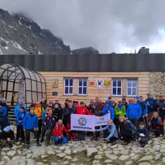 Grupa turystów pozuje do zdjęcia przed drewnianym schroniskiem górskim z flagą.