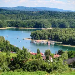 Malowniczy widok na jezioro z żaglówkami i lasem. Widać też domki letniskowe. Czy w Solinie można się kąpać? Tak, to idealne miejsce na wypoczynek!