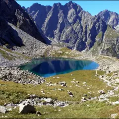 Górski, turkusowy Litworowy Staw na Słowacji, otoczony skalistymi zboczami i zieloną trawą.