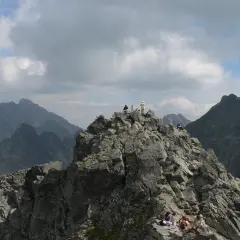 Grupa turystów odpoczywa na skalistym szczycie, podziwiając widok na Tatry. Trasa na Rysy jest wymagająca, ale widoki wynagradzają wysiłek.