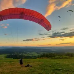 Szybowisko w Bezmiechowej o zachodzie słońca. Kilku paralotniarzy szybuje nad malowniczym krajobrazem.