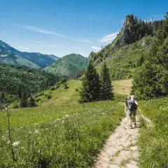 Turyści idą kamienistą ścieżką nad reglami, otoczeni zielonymi wzgórzami i skalistymi szczytami.