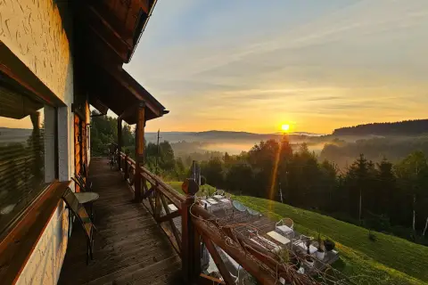 Drewniany taras z widokiem na mgliste Bieszczady o wschodzie słońca.