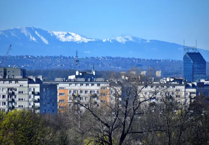 Widok na krakowskie bloki i wieżowiec. W oddali, na horyzoncie, widać ośnieżone szczyty Tatr.