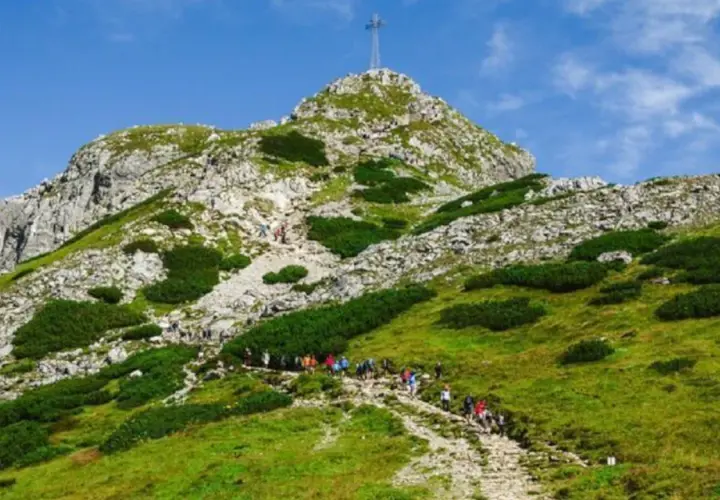 Tłum turystów podąża kamienistą trasą na Giewont. W oddali widać szczyt z krzyżem.