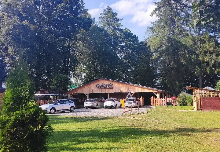 Drewniana restauracja Gwarek w Polańczyku, otoczona zielenią, z zaparkowanymi samochodami.