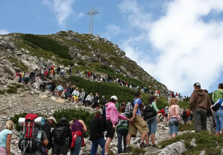 Tłum turystów podąża czerwonym szlakiem na Giewont. W oddali widoczny krzyż na szczycie.