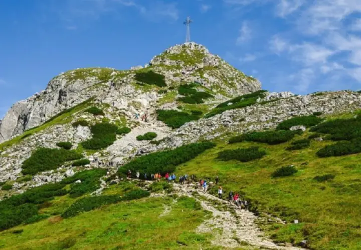 Grupa turystów wspina się kamienistym szlakiem na szczyt Giewontu w Tatrach. Góra przypomina śpiącego rycerza.