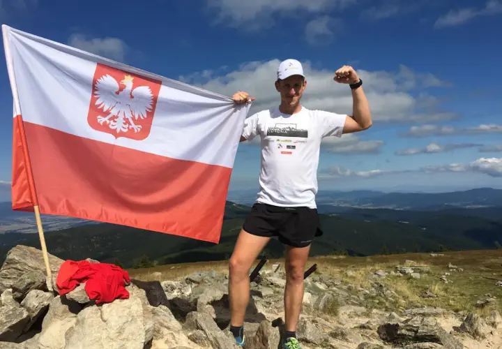Mężczyzna z polską flagą na szczycie górskim, świętuje zdobycie Korony Gór Polskich. Rekordowe osiągnięcie!