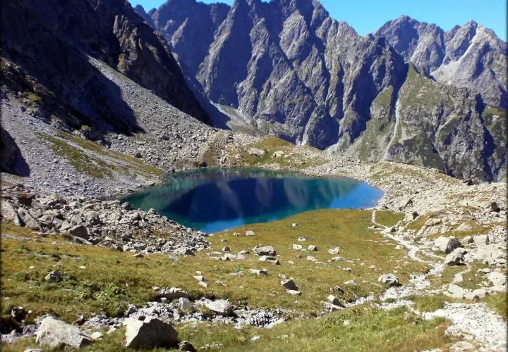Górski, turkusowy Litworowy Staw na Słowacji, otoczony skalistymi zboczami i zieloną trawą.