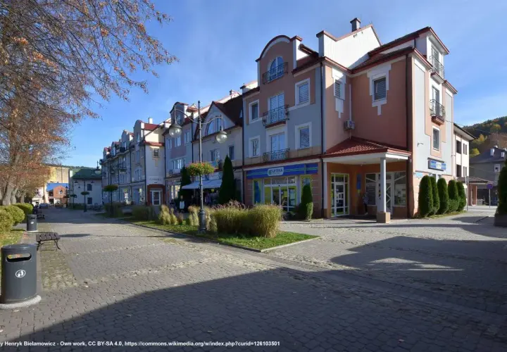 Urokliwy rynek w Ustrzykach Dolnych z kolorowymi kamienicami, zielenią i brukowanym deptakiem.