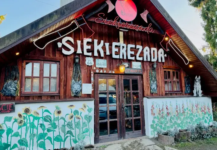 Karczma "Siekierezada" w Polańczyku, Bieszczady. Drewniana chata z neonem, rzeźbami wilków i malowidłami słoneczników.