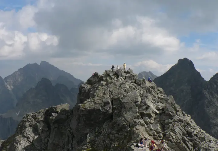 Grupa turystów odpoczywa na skalistym szczycie, podziwiając widok na Tatry. Trasa na Rysy jest wymagająca, ale widoki wynagradzają wysiłek.