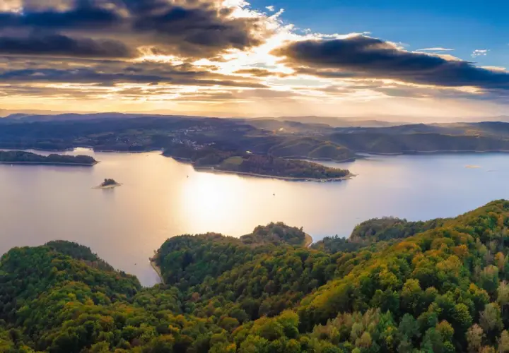 Widok z lotu ptaka na jezioro Solina otoczone zalesionymi wzgórzami o zachodzie słońca.