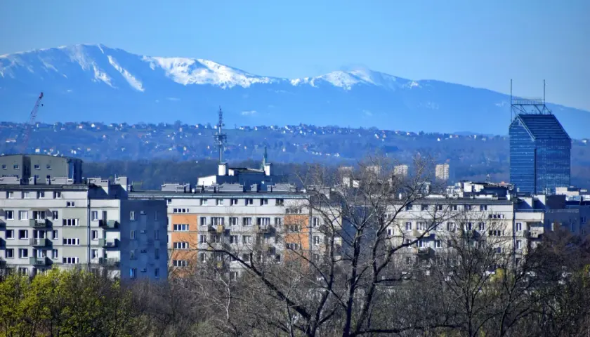 Widok na krakowskie bloki i wieżowiec. W oddali, na horyzoncie, widać ośnieżone szczyty Tatr.