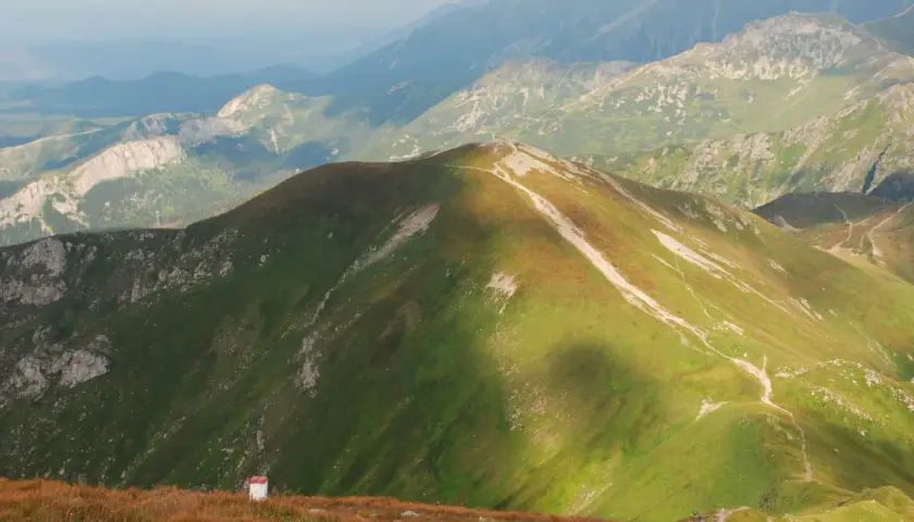 Widok na Tatry z Kopy Kondrackiej. Szlak turystyczny wije się po zielonych zboczach, a w oddali widać kolejne pasma górskie.