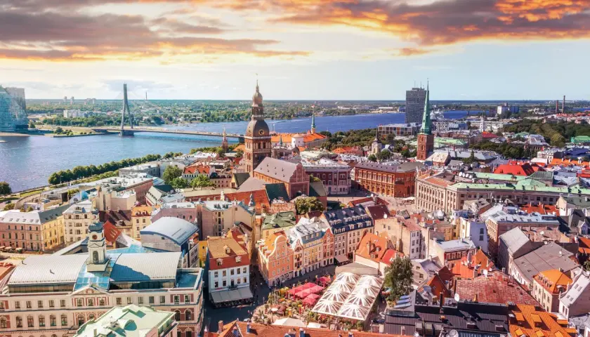 Widok na Rygę z lotu ptaka, z rzeką i mostem w tle. Widać urokliwe kamienice i place, idealne miejsca, by zastanowić się, co zjesc w Rydze.