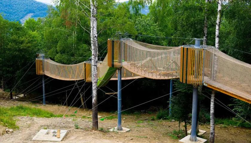 Drewniana kładka w koronach drzew, przypominająca zieloną plażę Polańczyka, w otoczeniu bujnej zieleni.