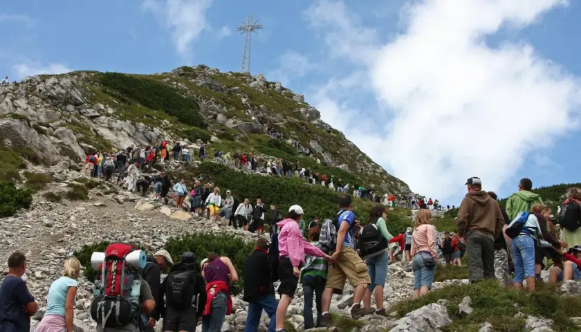 Tłum turystów podąża czerwonym szlakiem na Giewont. W oddali widoczny krzyż na szczycie.