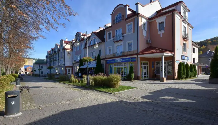 Urokliwy rynek w Ustrzykach Dolnych z kolorowymi kamienicami, zielenią i brukowanym deptakiem.