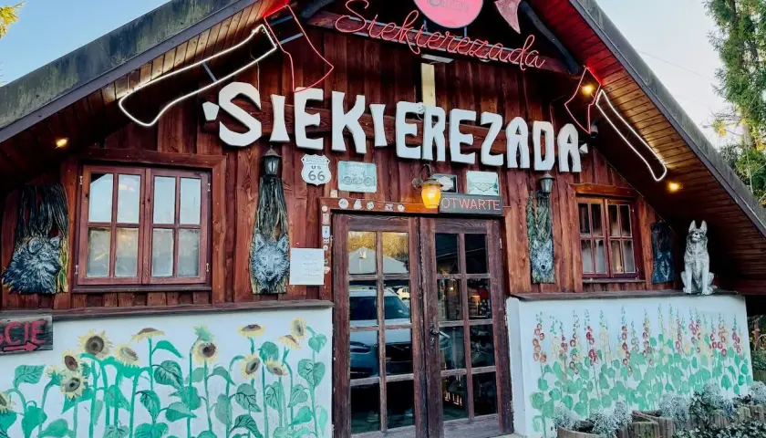 Karczma "Siekierezada" w Polańczyku, Bieszczady. Drewniana chata z neonem, rzeźbami wilków i malowidłami słoneczników.