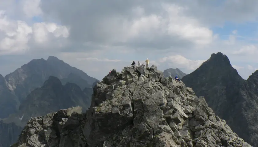Grupa turystów odpoczywa na skalistym szczycie, podziwiając widok na Tatry. Trasa na Rysy jest wymagająca, ale widoki wynagradzają wysiłek.