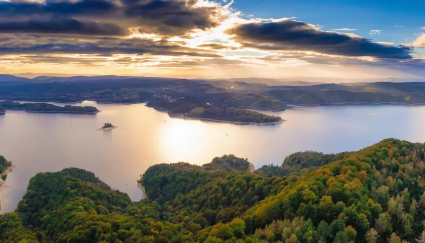 Widok z lotu ptaka na jezioro Solina otoczone zalesionymi wzgórzami o zachodzie słońca.
