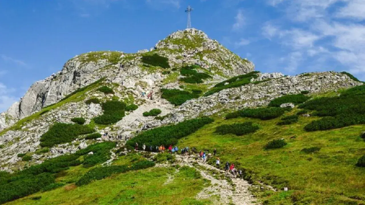 Tłum turystów podąża kamienistą trasą na Giewont. W oddali widać szczyt z krzyżem.
