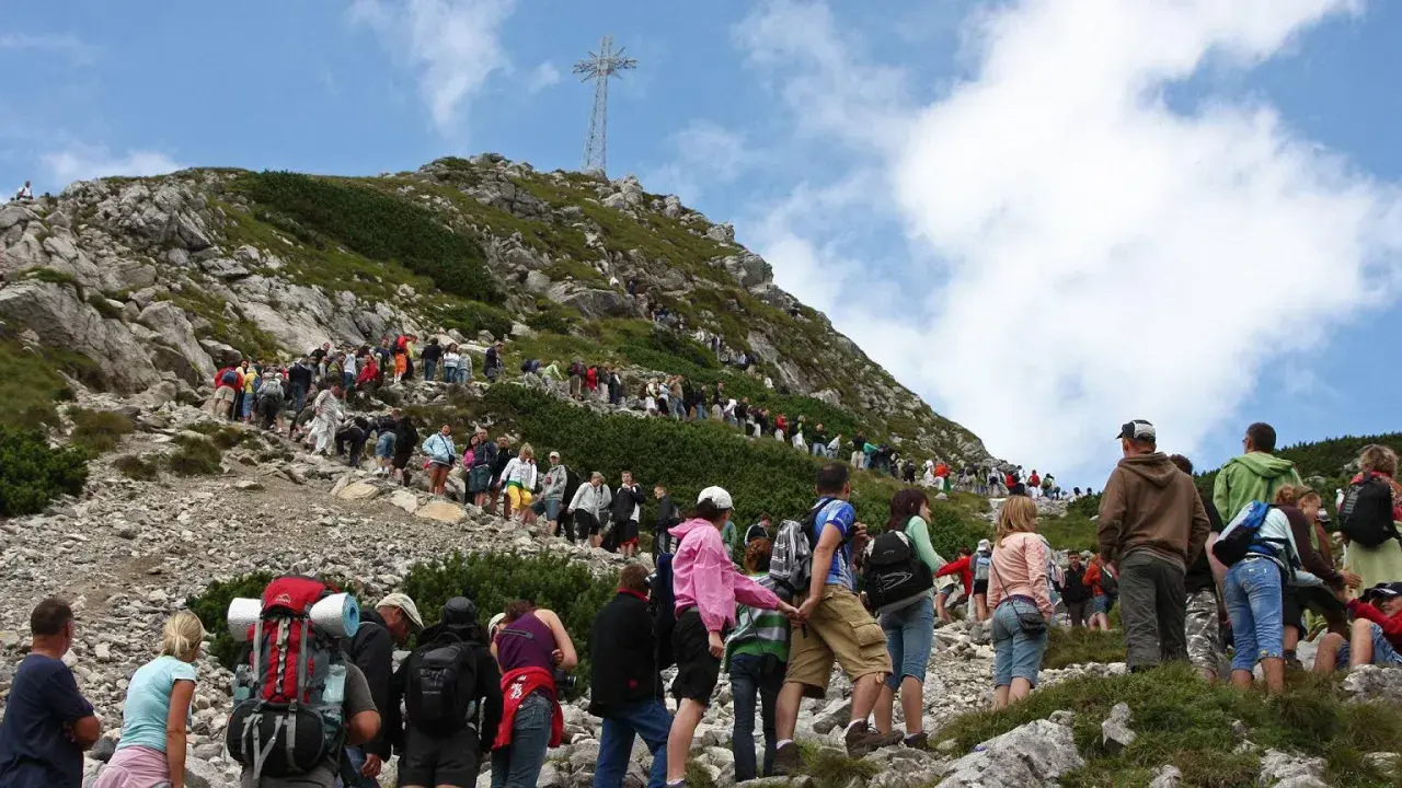 Tłum turystów podąża czerwonym szlakiem na Giewont. W oddali widoczny krzyż na szczycie.