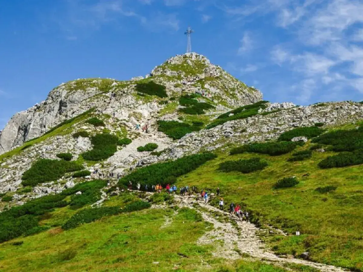 Grupa turystów wspina się kamienistym szlakiem na szczyt Giewontu w Tatrach. Góra przypomina śpiącego rycerza.