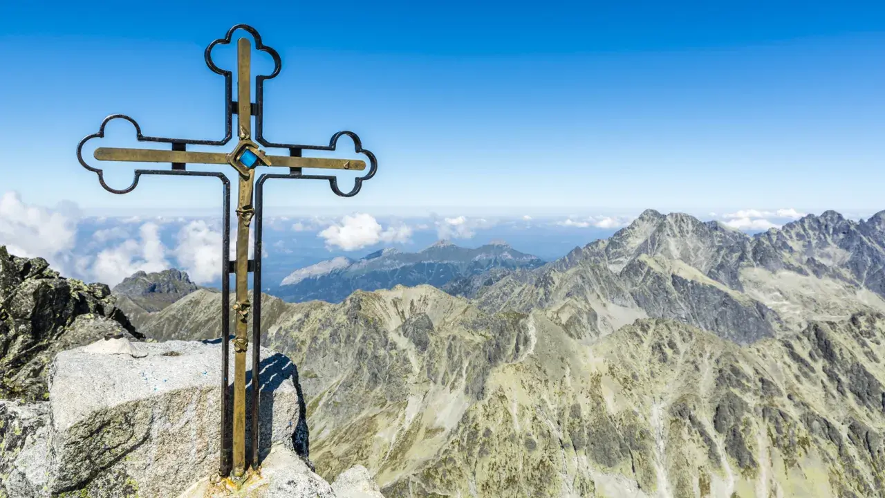 Krzyż na szczycie Gerlach bez przewodnika. Majestatyczne Tatry rozciągają się pod błękitnym niebem.