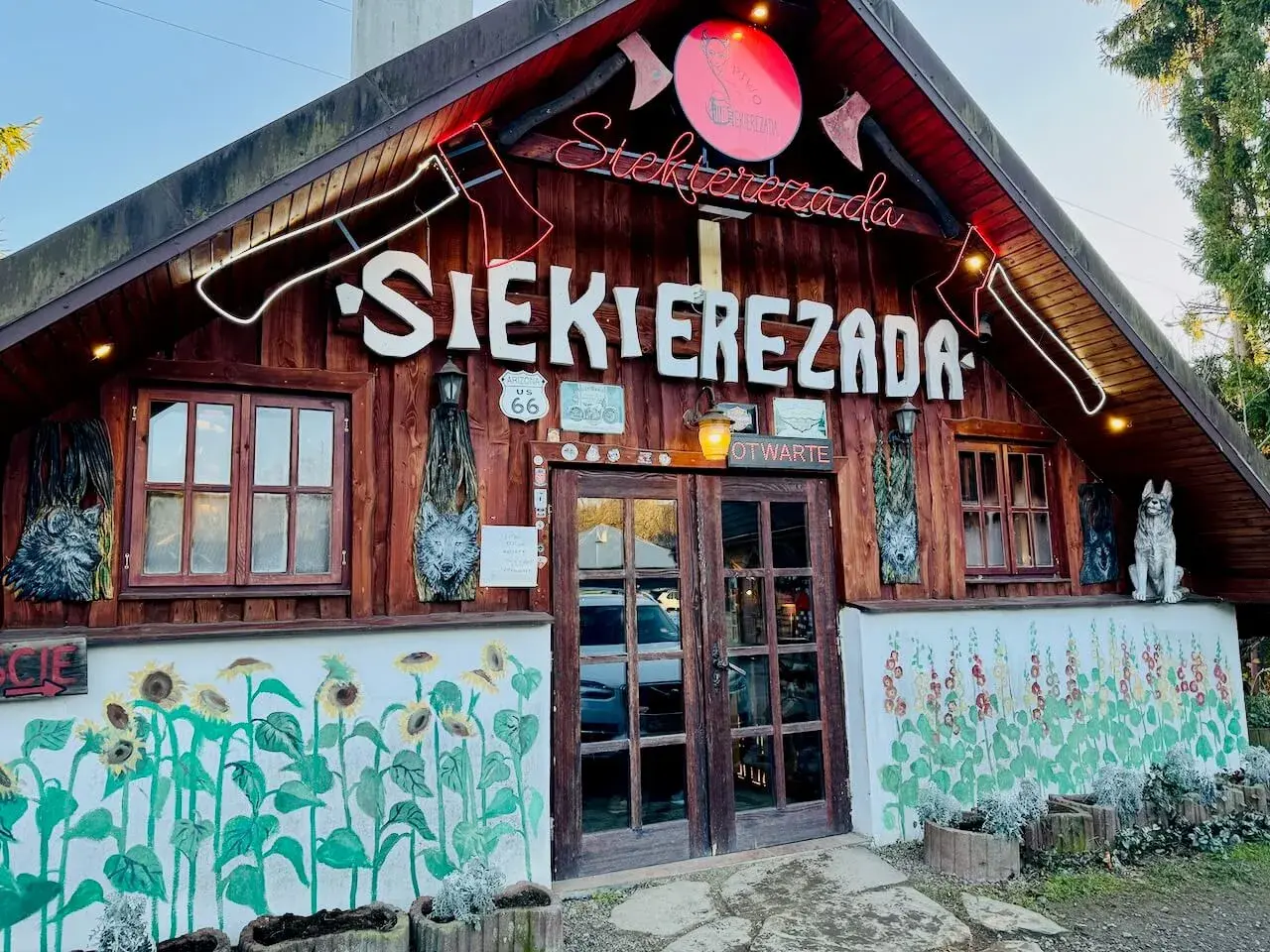 Karczma "Siekierezada" w Polańczyku, Bieszczady. Drewniana chata z neonem, rzeźbami wilków i malowidłami słoneczników.