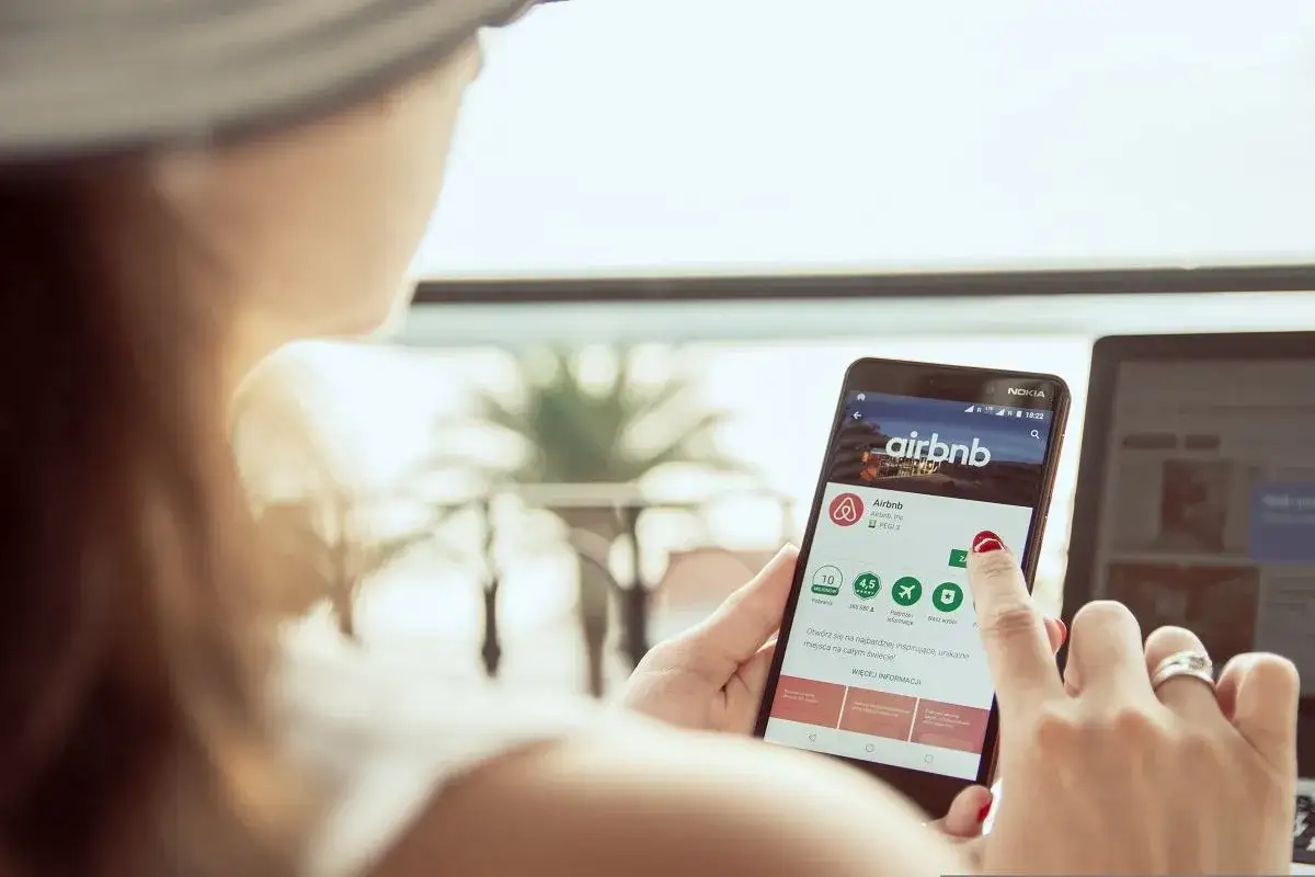 Kobieta szuka inspiracji, gdzie najlepiej rezerwować noclegi, przeglądając aplikację Airbnb na telefonie.