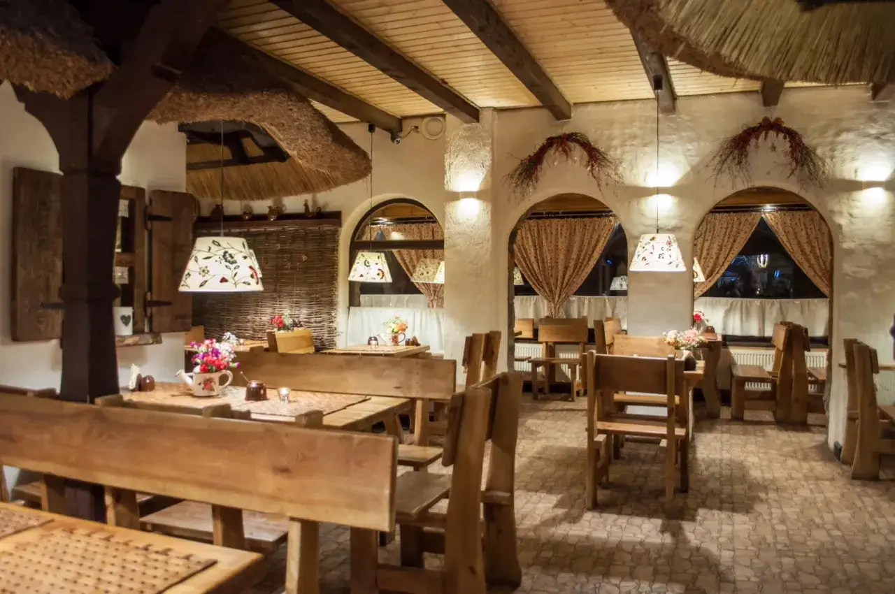 Przytulne wnętrze restauracji w Ustrzykach Dolnych, gdzie zjeść można w rustykalnym klimacie. Drewniane stoły, ławy i ozdobne lampy tworzą ciepłą atmosferę.