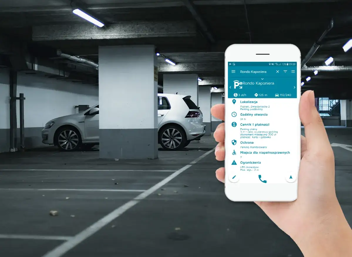 Smartfon pokazuje informacje o parkingu nad zaporą. W tle widać samochody na podziemnym parkingu.