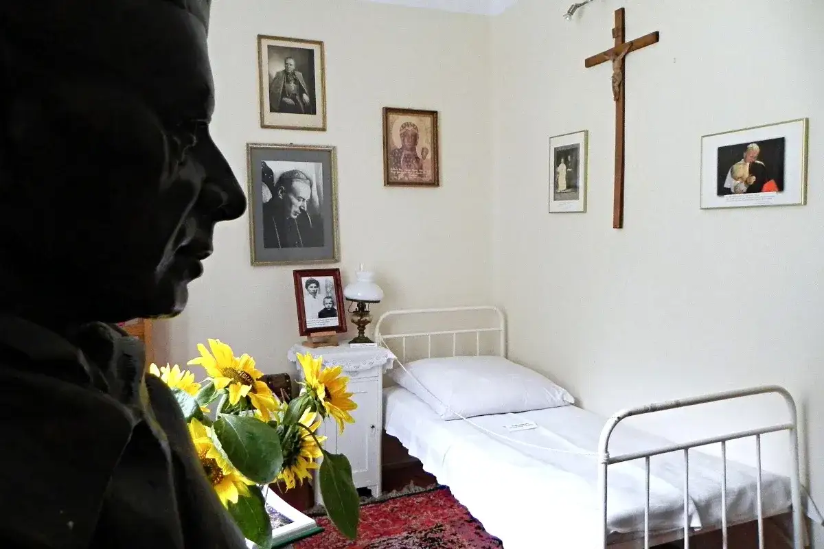 Pokój w klasztorze w Komańczy. Na ścianach wiszą portrety i krzyż. Na łóżku biała pościel.