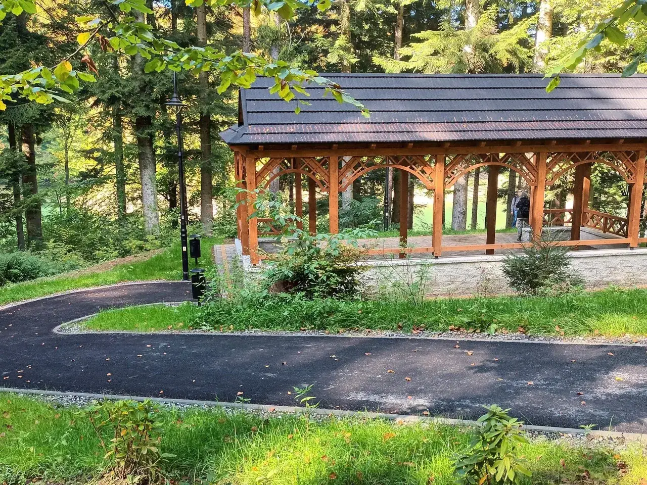 Drewniana altana w parku zdrojowym Polańczyk, otoczona lasem i ścieżką spacerową.