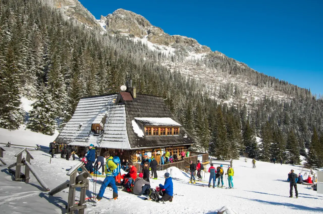 Ludzie w zimowym Tatrzańskim Parku Narodowym, gotowi do wędrówki po szlakach zimowych Tatry. Schronisko otoczone śniegiem i lasem.